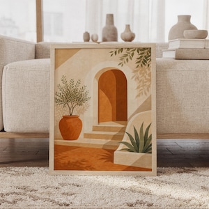Mediterranean arch wall art print of a sunlit terracotta arch with a curved stairway, a clay pot and leafy plants in sand, cream and olive tones, framed and leaning against a beige sofa on a textured rug in a bright Scandinavian living room.
