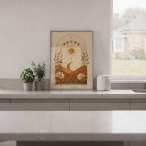 Celestial sun and moon wall art print leaning on the floor beside a cream armchair next to large garden windows.