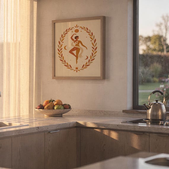 Framed terracotta goddess wall art hanging on a sunny kitchen wall next to a clean countertop and fruit bowl.