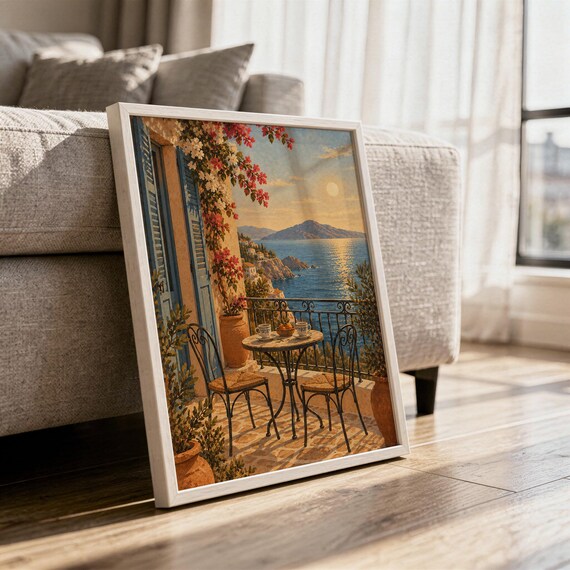 Mediterranean balcony wall art print in a white frame leaning against a gray sofa on a sunlit wooden floor.