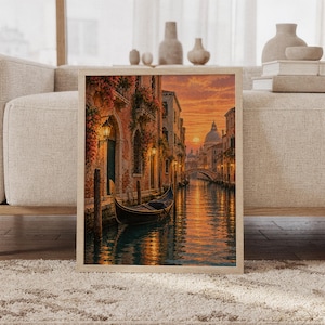 Venice canal sunset wall art print featuring glowing golden orange and peach skies, historic Venetian architecture, flower-covered facades, a gondola, and shimmering canal reflections in a painterly cityscape style, framed and leaning against a beige sofa on a textured rug in a bright Scandinavian living room.