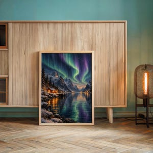 Aurora borealis mountain landscape wall art print leaning against a wooden cabinet by a teal wall beside a glowing floor lamp.