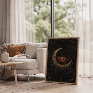 Vintage halloween moon wall art print leaning on the floor beside a cream armchair next to large garden windows.