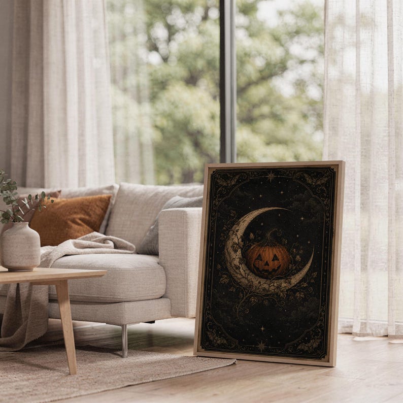 Vintage halloween moon wall art print leaning on the floor beside a cream armchair next to large garden windows.