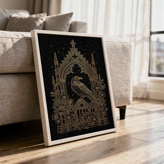 Gothic raven wall art print in a white frame leaning against a gray sofa on a sunlit wooden floor.