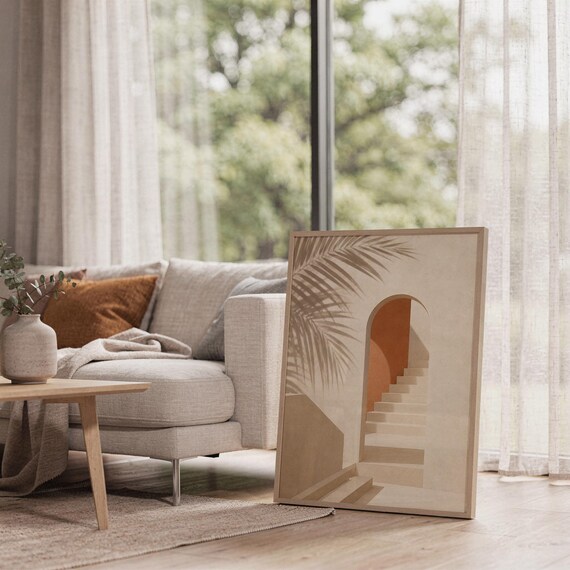 architectural artwork resting on the floor next to a grey sofa in a sunlit room.