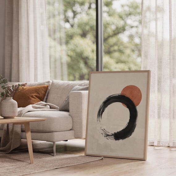 Framed abstract Ensō circle print standing on the floor in a sunlit living room near a beige sofa.