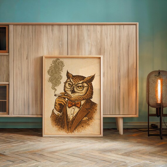A framed print of an owl in a brown suit, red bow tie, and glasses, smoking a cigar with smoke curling up, leans against a wall next to two white pillows and a wooden lamp.