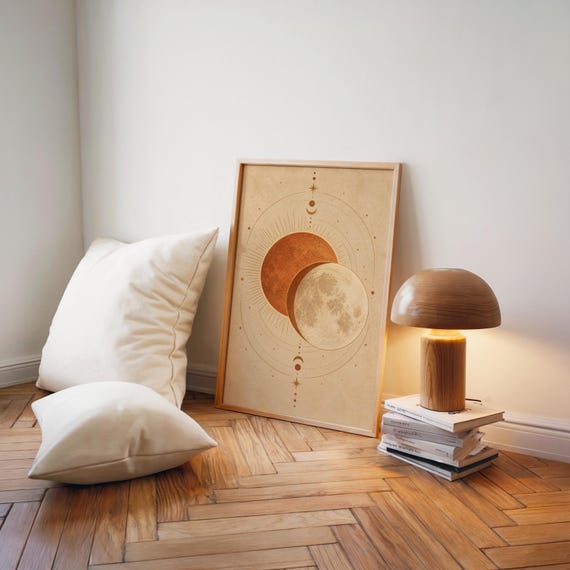 Sun and moon celestial wall art print leaning on a herringbone wood floor beside cream cushions and a wooden mushroom lamp.