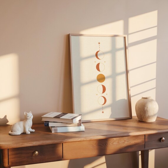 Vertical moon phases print on dark wooden desk with stacked books and sunlight