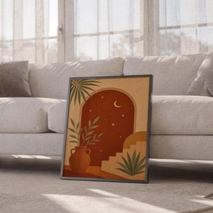 Terracotta moon and stars arch art print leaning against a white sofa in a bright living room with sheer curtains.
