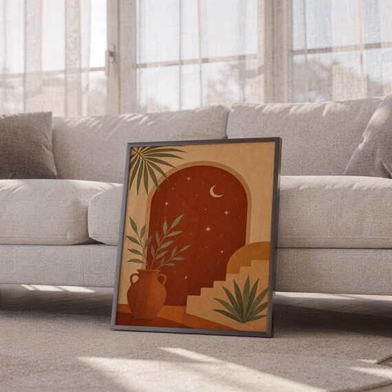 Terracotta moon and stars arch art print leaning against a white sofa in a bright living room with sheer curtains.