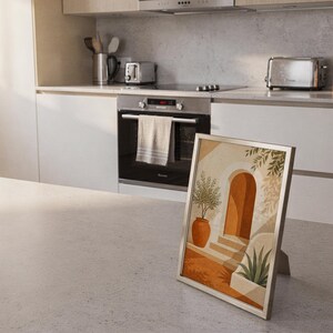 Mediterranean terracotta stairway arch print standing on a countertop in a modern white kitchen.