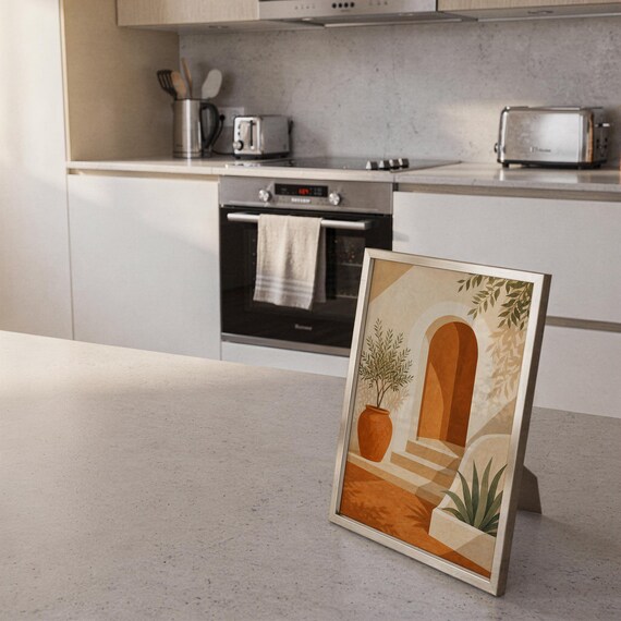 Mediterranean terracotta stairway arch print standing on a countertop in a modern white kitchen.