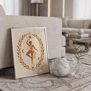 Minimalist framed dancing figure print leaning against a light beige sofa next to a decorative marble sphere on a rug.