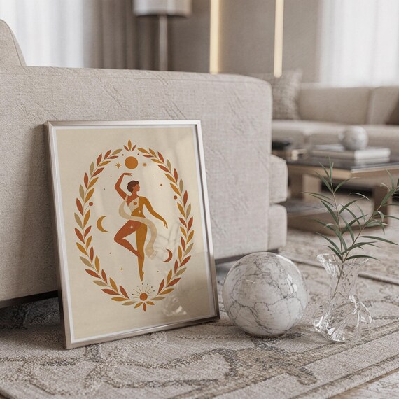 Minimalist framed dancing figure print leaning against a light beige sofa next to a decorative marble sphere on a rug.