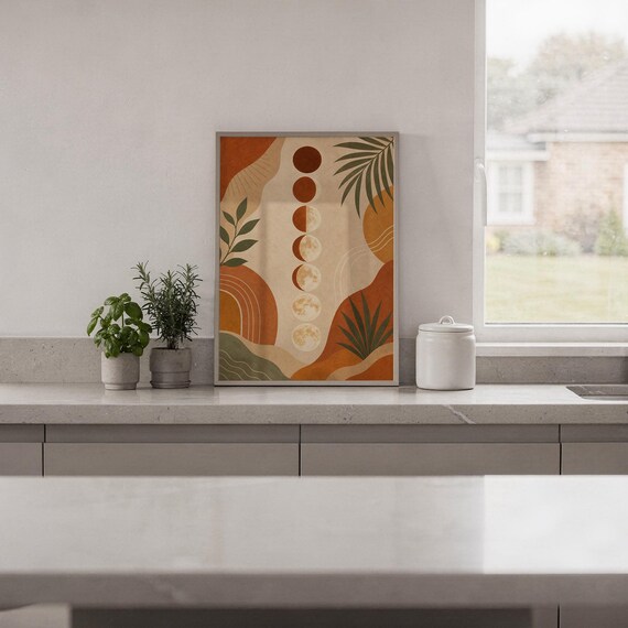 Boho moon phases art print standing on a white kitchen counter beside potted herbs.