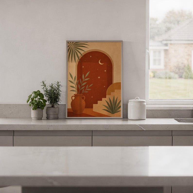Terracotta moon and stars arch art print standing on a white kitchen counter beside potted herbs.
