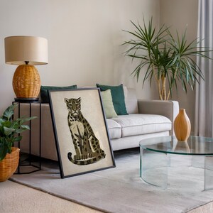 A framed print of a sitting leopard with dark green and brown spots on a light background, leaning against a light gray couch with a green pillow, next to a plant and a lamp.