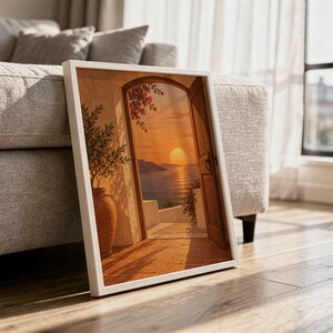 Mediterranean sunset doorway wall art print in a white frame leaning against a gray sofa on a sunlit wooden floor.