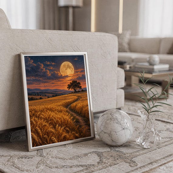 Moon wall art print in a silver frame leaning against a sofa beside a decorative marble sphere.