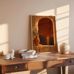Mediterranean night sea wall art print leaning on a wooden desk against a warm beige wall in soft window sunlight.