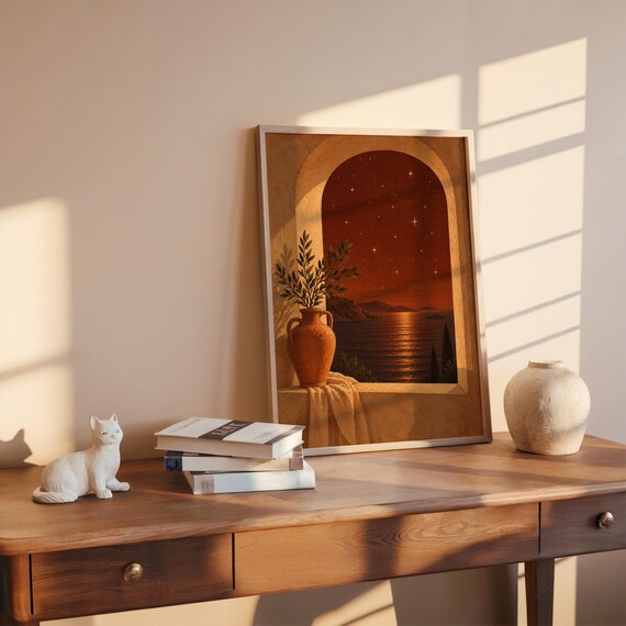 Mediterranean night sea wall art print leaning on a wooden desk against a warm beige wall in soft window sunlight.