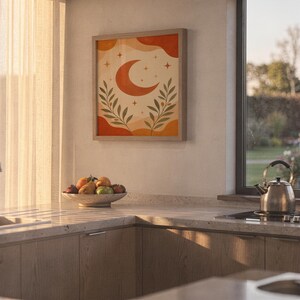 Terracotta crescent moon and olive branch print hanging above a stone countertop with a fruit bowl in a sunny kitchen.