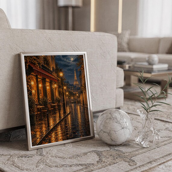Paris eiffel tower wall art print in a silver frame leaning against a sofa beside a decorative marble sphere.