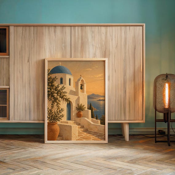 Santorini church wall art print leaning against a wooden cabinet by a teal wall beside a glowing floor lamp.