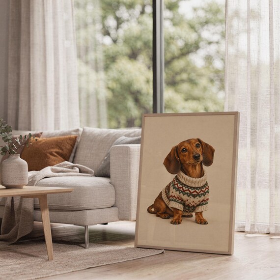 Dachshund sweater wall art print in a white frame leaning against a gray sofa on a sunlit wooden floor.