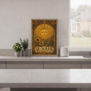 Art nouveau sunflower wall art print in a white frame leaning against a gray sofa on a sunlit wooden floor.