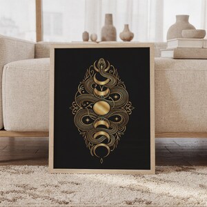 Gold snake moon phase wall art print featuring intricate metallic gold snakes, crescent moons, stars, and ornamental botanical details on a deep black background, framed and leaning against a beige sofa on a textured rug in a bright Scandinavian living room.