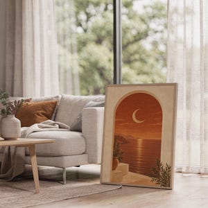 Mediterranean crescent moon arch print leaning on the floor beside a cream armchair next to large garden windows.
