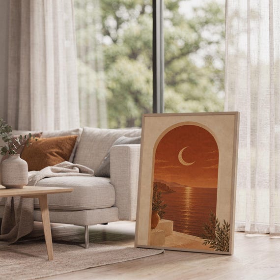 Mediterranean crescent moon arch print leaning on the floor beside a cream armchair next to large garden windows.