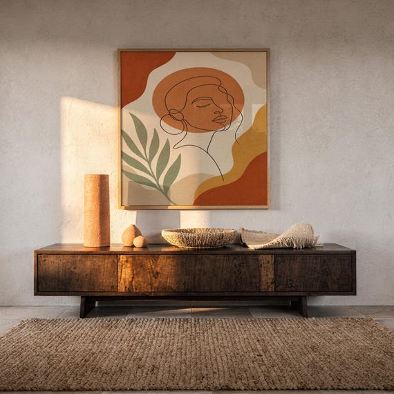 Abstract line art face print hanging above a dark wood console and jute rug in a warm neutral interior.
