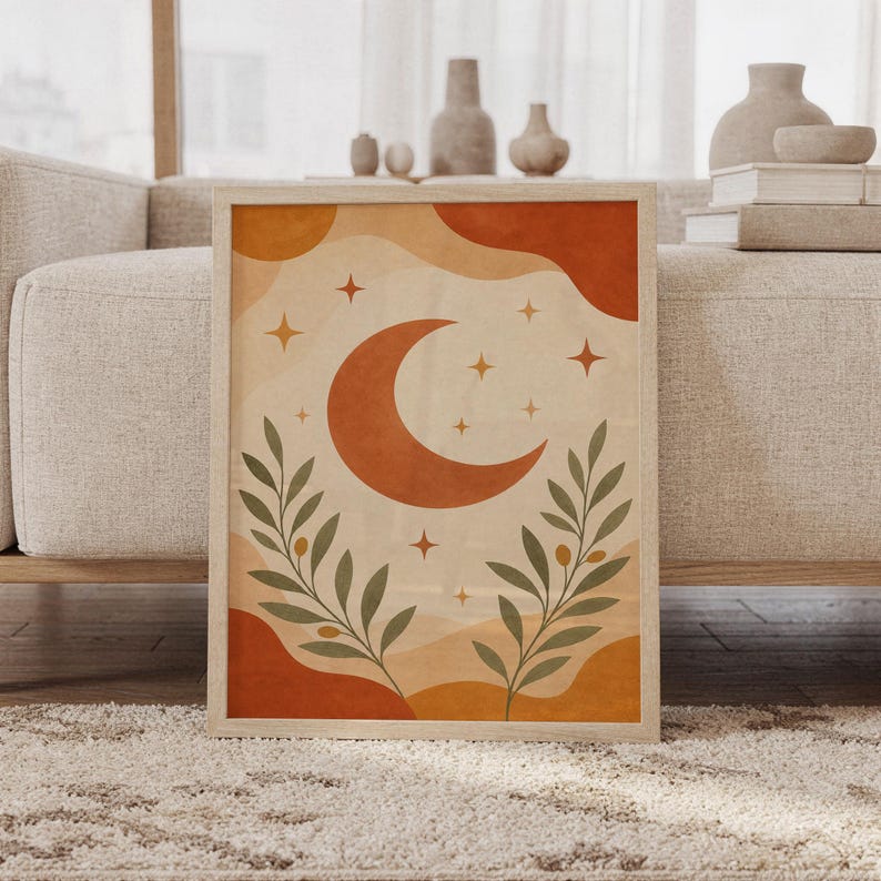 Celestial moon wall art print of a terracotta crescent moon with golden stars and olive branches over abstract cream, ochre and rust shapes, framed and leaning against a beige sofa on a textured rug in a bright Scandinavian living room.