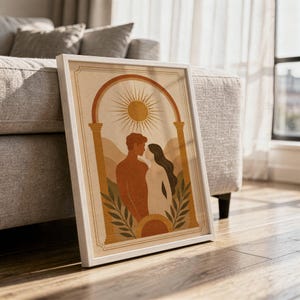 Framed terracotta love silhouette poster leaning on a light wooden floor against a cozy living room sofa in warm morning sunlight.