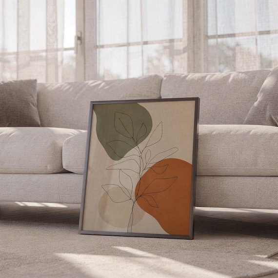 Black framed minimalist botanical print resting on the floor beside a white sofa.