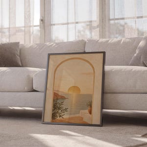 Mediterranean sunset arch print leaning against a white sofa in a bright living room with sheer curtains.