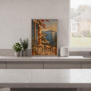 Mediterranean balcony wall art print standing on a white kitchen counter beside potted herbs.