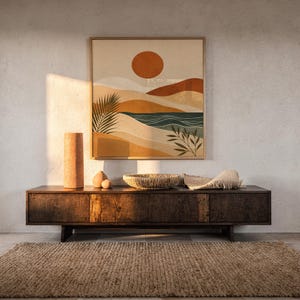 Framed modern abstract landscape print on dark wooden console table in a bright sunlit room.