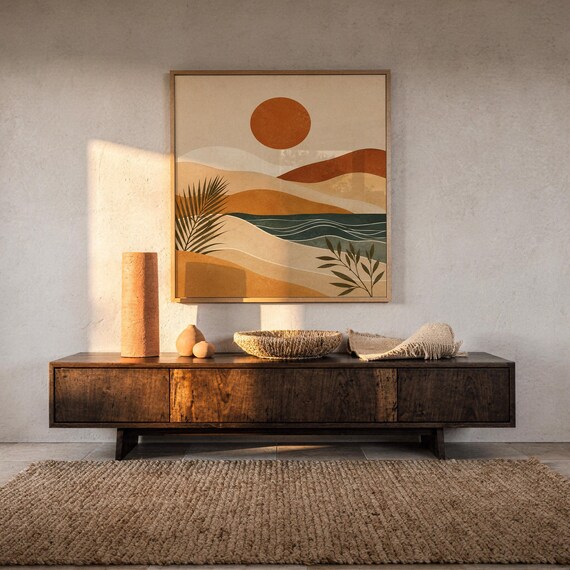 Framed modern abstract landscape print on dark wooden console table in a bright sunlit room.