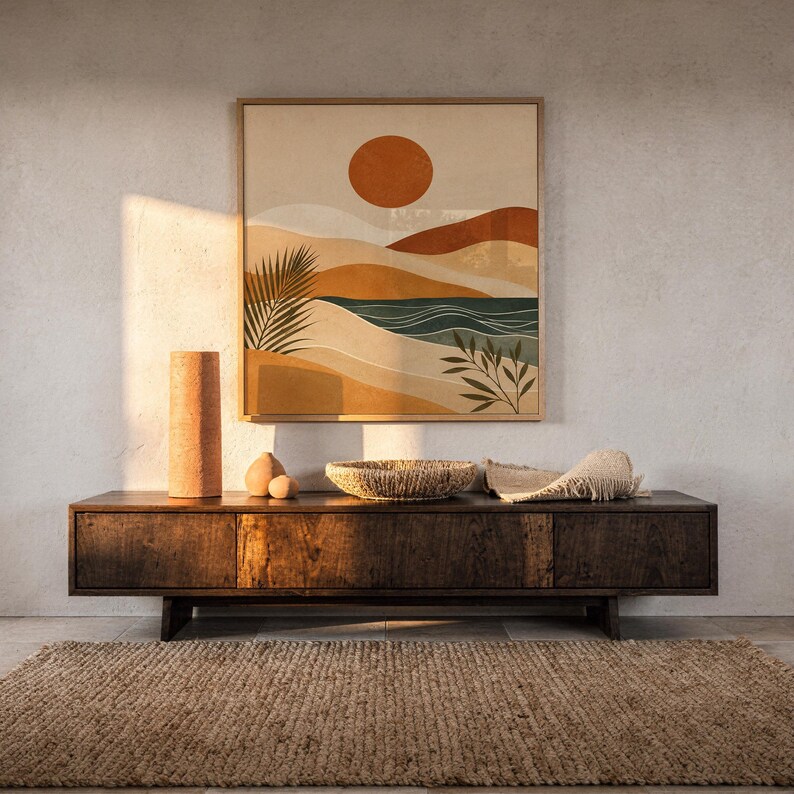 Framed modern abstract landscape print on dark wooden console table in a bright sunlit room.