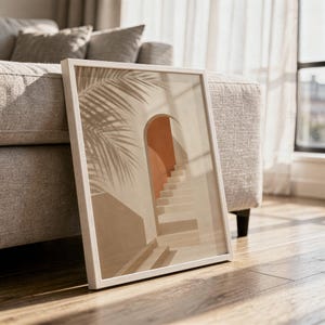Close-up of a framed palm and arch print leaning on a light-colored wooden floor.