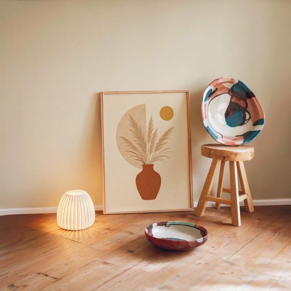 Single framed pampas grass artwork leaning on a wooden floor in a warm, cozy room.