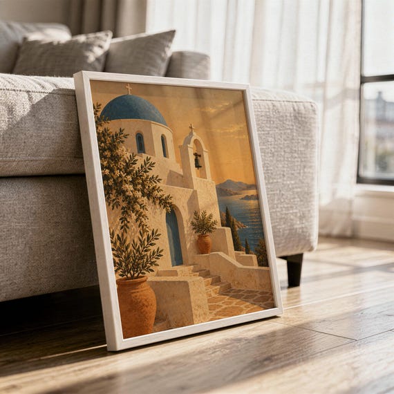 Santorini church wall art print in a white frame leaning against a gray sofa on a sunlit wooden floor.