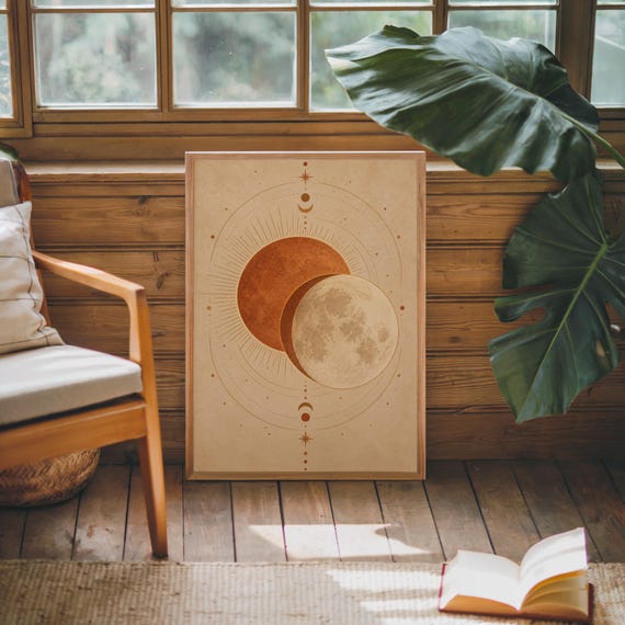 Sun and moon celestial wall art print leaning against warm wood paneling beside a wooden armchair and a monstera plant.