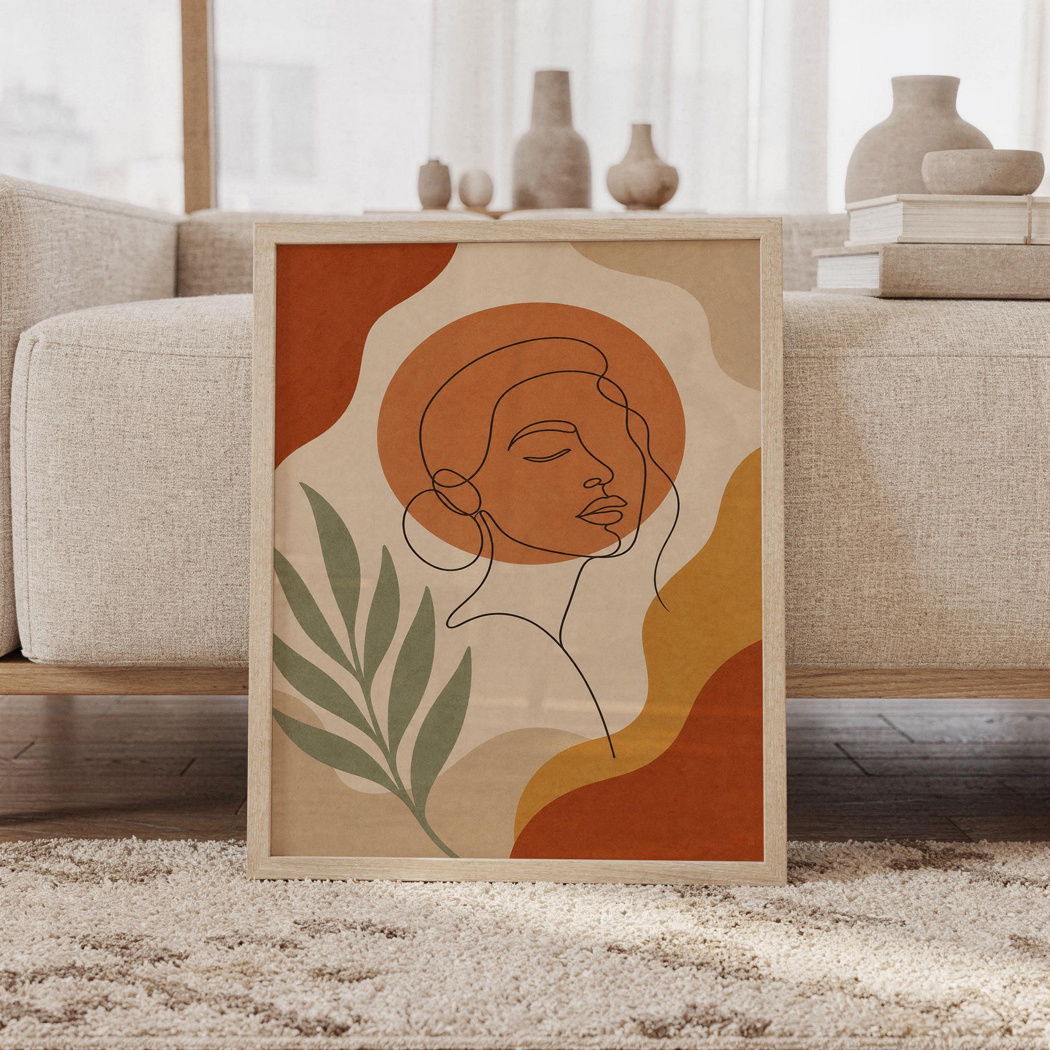 Abstract line art woman wall art print of a continuous line drawing of a woman's face with organic shapes and leaves in terracotta, ochre, cream and sage, framed and leaning against a beige sofa on a textured rug in a bright Scandinavian living room.