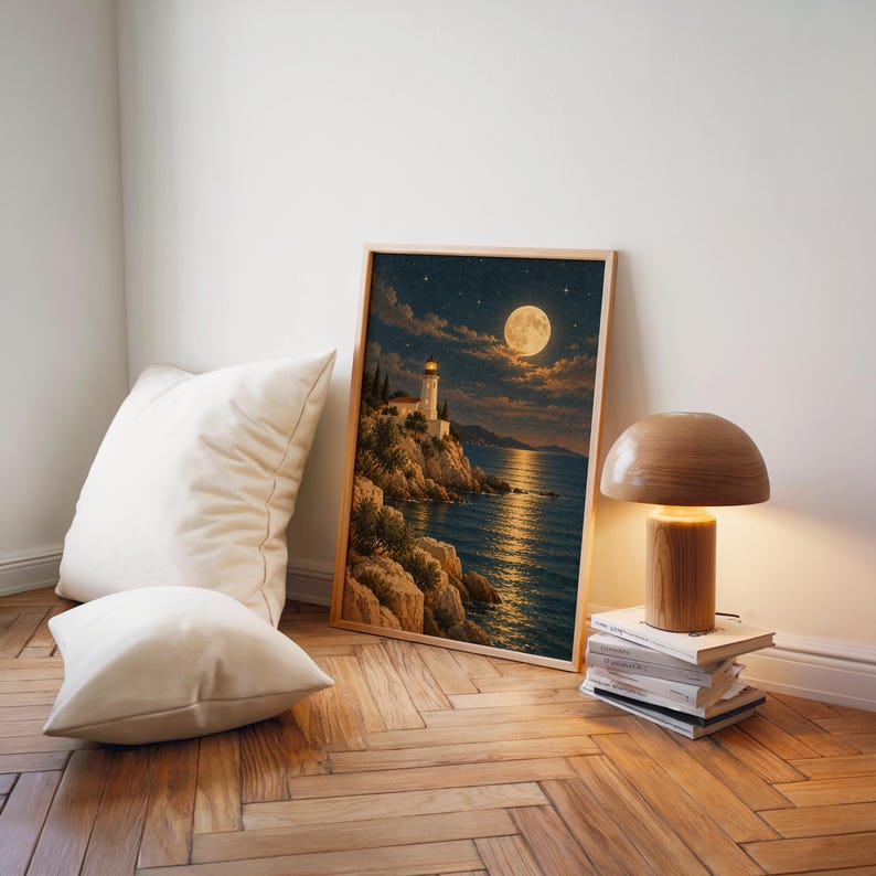 Moonlit lighthouse wall art print leaning on a herringbone wood floor beside cream cushions and a wooden mushroom lamp.
